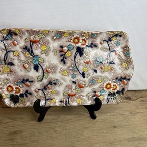 May include: A vintage ceramic serving tray with a scalloped edge and a floral pattern in shades of blue, yellow, orange, and brown on a white background.