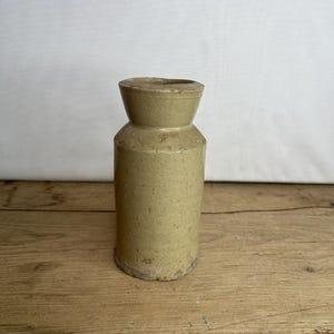 Könnte beinhalten: Ein zylindrisches Vintage-Steinzeuggefäß in einem hellgrün-gelben Farbton. Das Gefäß hat einen schmalen Hals und einen breiteren Boden mit einer leicht rauen, gealterten Textur. Die Gesamthöhe beträgt ca. 15 cm.