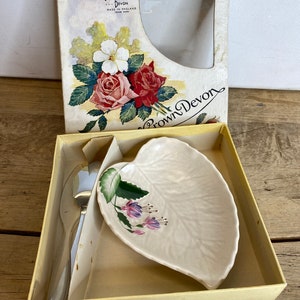 Op de afbeelding: Een wit keramisch bladvormig schaaltje met een bloemenmotief en een zilveren serveerschep in een gele doos. De doos heeft een label met de tekst "Crown Devon Made in England Trade Mark".