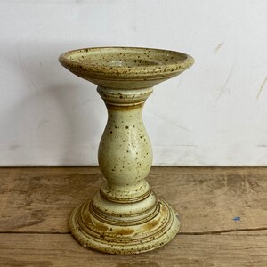 Peut inclure: Un bougeoir en céramique beige moucheté, avec un dessus large et peu profond et une base en piédestal arrondie. Le bougeoir a une base circulaire, une section médiane bulbeuse et une surface légèrement texturée. Hauteur totale d'environ 18 cm.