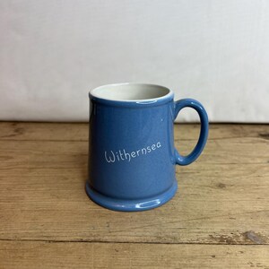 May include: A blue ceramic mug with a white handle and the word "Withernsea" written on the front.