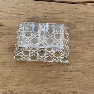 May include: A clear, rectangular crystal trinket box with a geometric diamond pattern. The box has a lid with two compartments and sits on a wooden surface. The box is designed to hold small items.