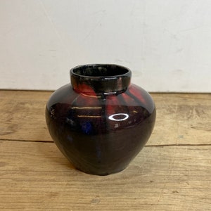 Puede incluir: Un jarrón pequeño, redondo, de cerámica negra con esmalte rojo y verde. El jarrón tiene un acabado brillante.