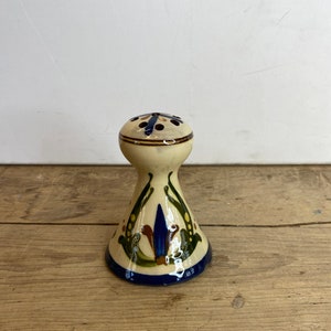 May include: A ceramic salt shaker with a cream-colored base and a blue, green, and brown floral design. The top is cream-colored with several small holes and a blue and brown pattern. The base is a dark blue.