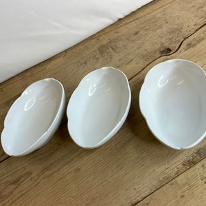 Puede incluir: Un conjunto de tres jarrones de cerámica de diferentes alturas y formas. El jarrón más alto es de color beige claro, el del medio marrón oscuro y el más pequeño blanco moteado. Cada jarrón tiene un acabado liso y mate.