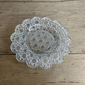 May include: A clear glass saucer with a scalloped edge and intricate geometric pattern. The saucer is perfect for serving small snacks or desserts.