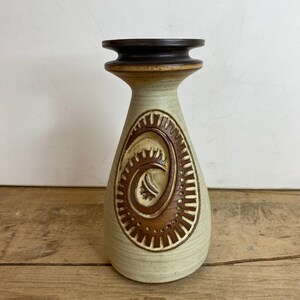 May include: A ceramic vase with a beige body and a dark brown top. The vase features a raised, spiral design in brown. The vase has a unique shape, wider at the base and tapering towards the top.