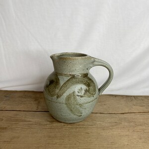 May include: A white ceramic mug with a black handle and the text "But First, Coffee" in a black, bold font. The mug is sitting on a white surface. The mug is approximately 4 inches tall.