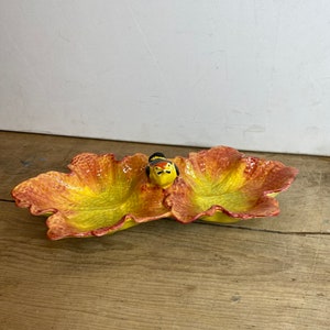 May include: A ceramic leaf-shaped serving dish with a yellow and orange gradient. The dish has two compartments and a small bird figurine in the centre. The dish is likely used for serving snacks or appetizers.