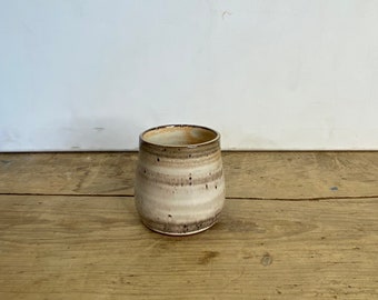 May include: A handmade ceramic tumbler with a speckled, layered design in shades of beige, brown, and white. The cup has a slightly flared shape and a smooth, glazed finish. The rim is a darker brown.