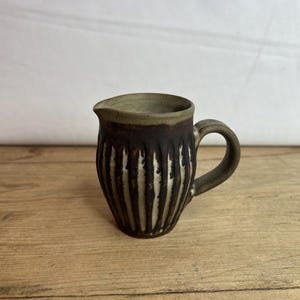 May include: A small, brown and white ceramic pitcher with a ribbed design. The pitcher has a handle and a spout.