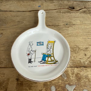 Pode incluir: Prato de cerâmica branco em forma de frigideira com alça. O prato apresenta uma ilustração de desenho animado de dois homens, um em pé e outro sentado em uma cadeira de balanço. O texto "You and your "Once More for Old Time's Sake" está impresso na parte inferior do prato.
