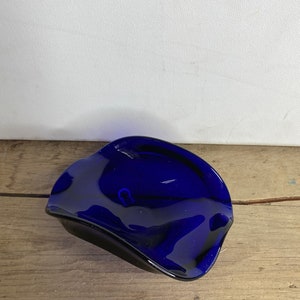 May include: A cobalt blue glass ashtray with a wavy, organic shape.