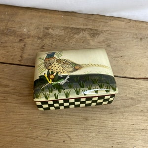 Puede incluir: Una caja cuadrada de cerámica con un diseño pintado de un faisán de pie en un campo de hierba. La caja tiene un patrón de cuadros negros y blancos en la parte inferior.
