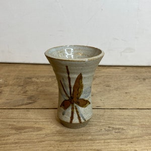 May include: A small, white ceramic vase with a brown and blue butterfly design.