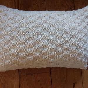 May include: A white knitted pillow with a diamond pattern. The pillow is soft and fluffy, and would be perfect for adding a touch of comfort to any room.