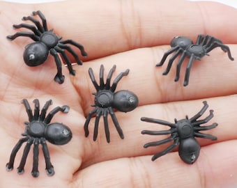 May include: Five small, black plastic spiders with detailed legs and body segments. These Halloween decorations are displayed on a light background, perfect for crafting or spooky displays.