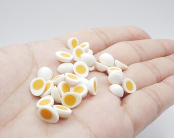 May include: A hand holding a pile of white and yellow miniature plastic eggs. The eggs are halved and show a yellow yolk inside.