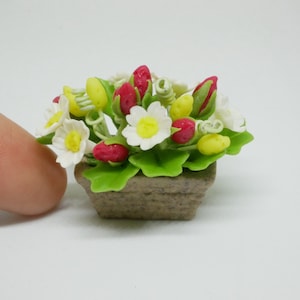 May include: A miniature flower arrangement in a brown planter. The flowers are white with yellow centers and red buds. The arrangement is made of polymer clay.