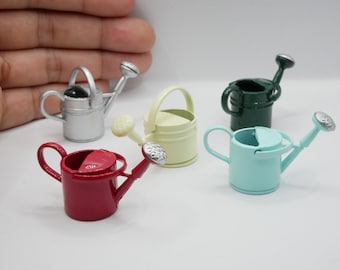 May include: Five miniature metal watering cans in different colors: silver, yellow, green, blue, and red. The watering cans have a spout and a handle.