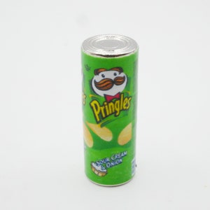 Pu&ograve; includere: Una lattina di Pringles verde e gialla con un coperchio bianco. La lattina ha un personaggio dei cartoni animati con i baffi e un papillon. Il testo sulla lattina dice "Pringles" e "Sour Cream & Onion".