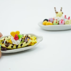 May include: A miniature banana split dessert with chocolate sauce, whipped cream, and colorful fruit toppings. The dessert is served on a white ceramic dish.