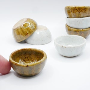 May include: A set of six small ceramic bowls, some are white with brown speckles and some are brown with white speckles.