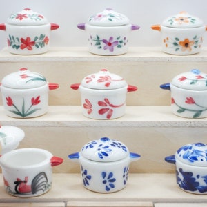 May include: Nine miniature ceramic pots with lids, each decorated with different floral and geometric patterns in shades of red, blue, and white. The pots are arranged on a tiered wooden display stand.