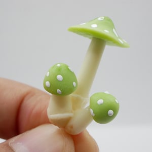 May include: A miniature mushroom sculpture with a light green cap and white polka dots. The stem is off-white. The sculpture is a whimsical decorative item.