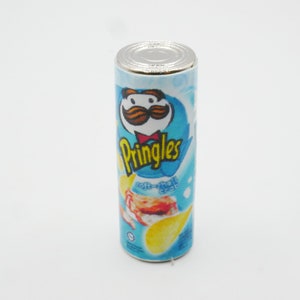 Pu&ograve; includere: Una lattina di patatine Pringles blu e bianca con un baffo rosso e bianco sul davanti. La lattina dice "Pringles" in lettere bianche e "Crema acida e cipolla" in lettere bianche pi&ugrave; piccole.