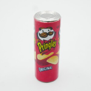 Pu&ograve; includere: Una lattina rossa e bianca di patatine Pringles Original. La lattina presenta un personaggio dei cartoni animati con i baffi e una patatina.