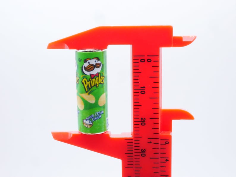 Pu&ograve; includere: Uno strumento di misurazione in plastica rossa con un contenitore di patatine Pringles verde e giallo all'interno. La lattina &egrave; etichettata "Pringles Sour Cream & Onion".