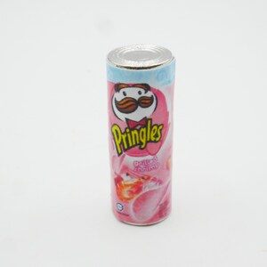 Pu&ograve; includere: Una lattina di patatine Pringles rosa e bianca con un personaggio dei cartoni animati con i baffi e il testo "Pringles" e "Gamberi alla griglia".