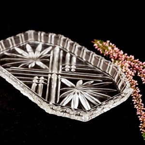 Könnte beinhalten: Ein klares Glasserviertablett mit einem geschliffenen Glasdesign. Das Tablett hat eine rechteckige Form mit abgerundeten Ecken und einem gewellten Rand. Das Tablett ist mit einem sich wiederholenden Muster aus Sternen und Linien verziert.