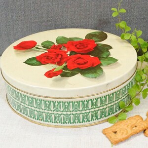 Peut inclure: Boîte à biscuits vintage ronde en métal avec une bordure verte et dorée. Le couvercle présente un motif floral avec des roses rouges et des feuilles vertes sur fond blanc.