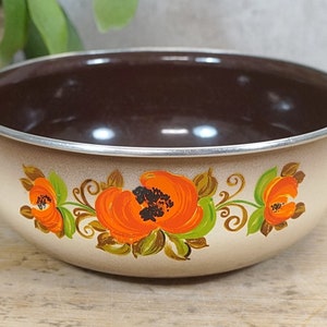Könnte beinhalten: Eine vintage Emaille-Schüssel mit braunem Innenraum und beigefarbenem Außenraum. Die Schüssel hat ein Blumenmuster mit orangefarbenen, grünen und braunen Blumen.