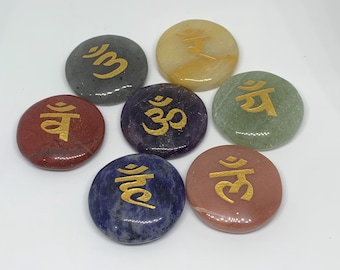 Puede incluir: Siete piedras redondas y pulidas de varios colores, cada una con un símbolo dorado. Las piedras están dispuestas en un patrón circular. Los colores incluyen rojo, azul, verde, morado, gris, amarillo y marrón. Los símbolos parecen ser de origen oriental.