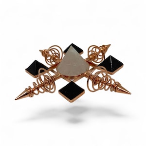 May include: A copper-colored orgone pyramid with a clear quartz crystal pyramid at the center, surrounded by four black obsidian pyramids. The design includes copper coils and pointed tips, creating a geometric and spiritual aesthetic.
