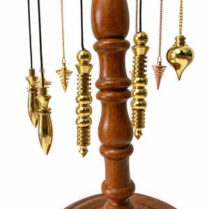 Peut inclure: Un support en bois avec un montant central tourné soutient plusieurs pendules suspendus. Les pendules sont fabriqués en métal poli doré et cuivré, présentant diverses formes géométriques, notamment des designs en goutte, coniques et cylindriques.