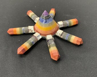 Könnte beinhalten: Ein farbenfroher Chakra-Energiegenerator mit einer zentralen Pyramide und sieben ausstrahlenden Kristallspitzen. Die Pyramide weist farbige Bänder auf, und die Kristallspitzen sind mit silberfarbenem Metall bedeckt.