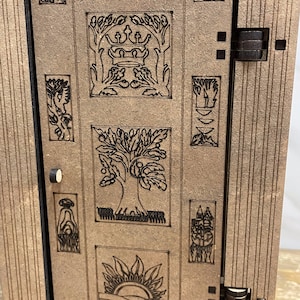 Op de afbeelding: Een houten deur met een decoratief ontwerp met een boom, een kroon, een zon en andere symbolen. De deur is gesloten en heeft een kleine knop aan de linkerkant.