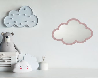 May include: A nursery decor scene featuring a cloud-shaped mirror with a pink border, a gray bear plush toy, and a cloud-shaped light fixture. A white shelf holds a white box, a cloud-shaped night light, and a small white container.