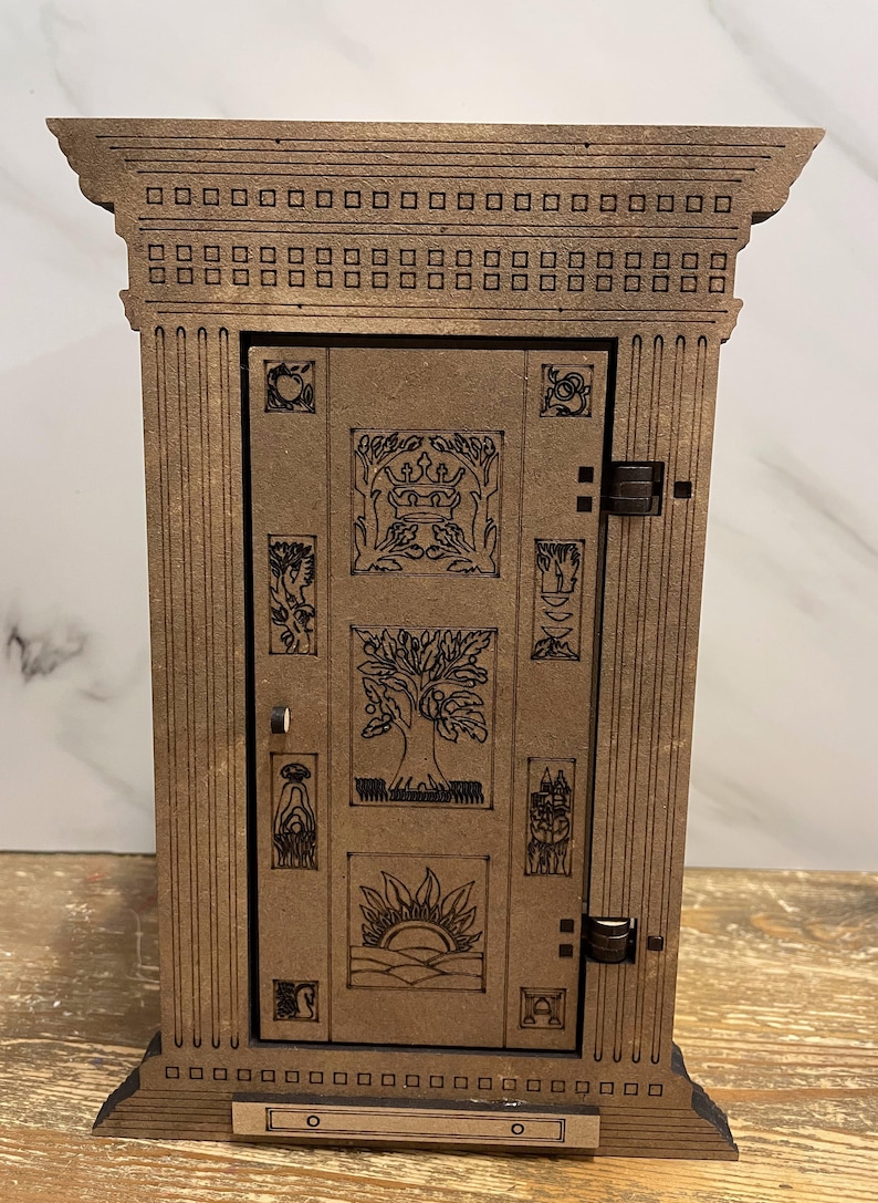 Op de afbeelding: Een houten doos met een decoratieve deur met ingewikkelde houtsnijwerk van bomen, kronen en andere symbolen. De doos heeft een bruine afwerking en een eenvoudig ontwerp.