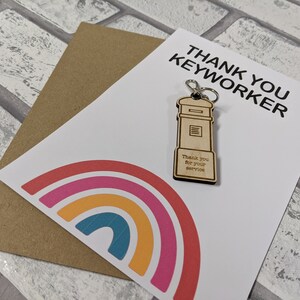 Könnte beinhalten: Eine weiße Karte mit einem Regenbogen-Design und dem Text "Thank You Keyworker". Ein Holzschlüsselanhänger mit einem roten Briefkasten-Design und dem Text "Thank you for your service" ist an der Karte befestigt.