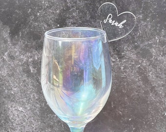 May include: A clear glass wine glass with a heart-shaped acrylic place card that says "Sarah" on it.