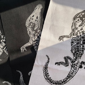 May include: Two black fabric patches with a white skeletal lizard design. The lizard on the right patch is curled into a circle.
