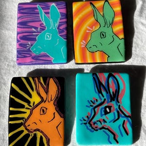 May include: Four rectangular art pieces featuring rabbit profiles. Each piece has a different color scheme: purple and teal, orange and yellow, black and orange, and teal with red and blue outlines. The rabbit designs are stylized and modern.