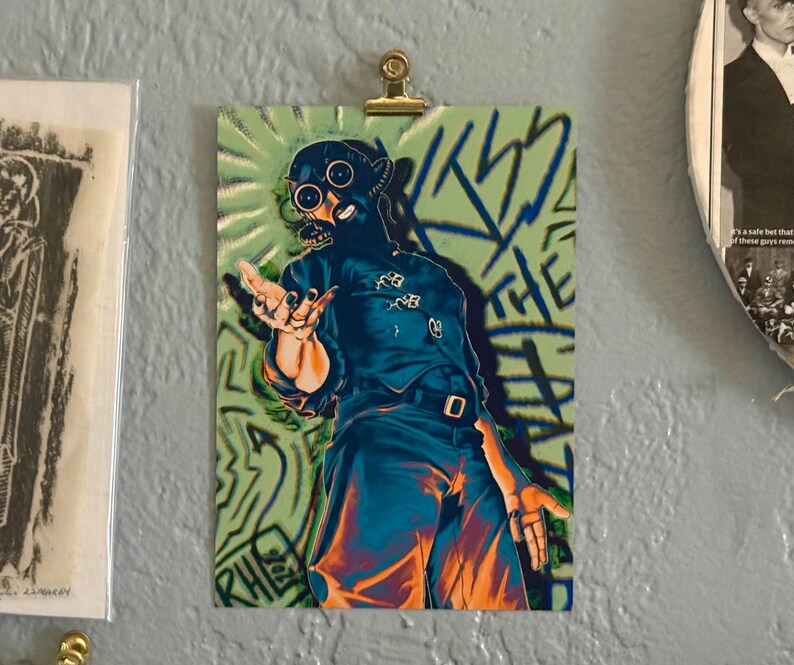 Pode incluir: Uma impress&atilde;o art&iacute;stica retangular apresentando uma figura usando uma m&aacute;scara de g&aacute;s escura e um uniforme correspondente com cinto. A figura posa com as m&atilde;os estendidas contra um fundo verde claro com texto azul estilo grafite KISS THE PAIN.