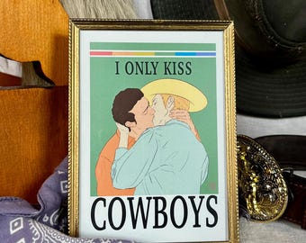 Pode incluir: Uma impressão artística emoldurada com uma moldura dourada. A impressão apresenta uma ilustração de dois cowboys se beijando, com o texto "I ONLY KISS COWBOYS" em negrito. O fundo é verde.