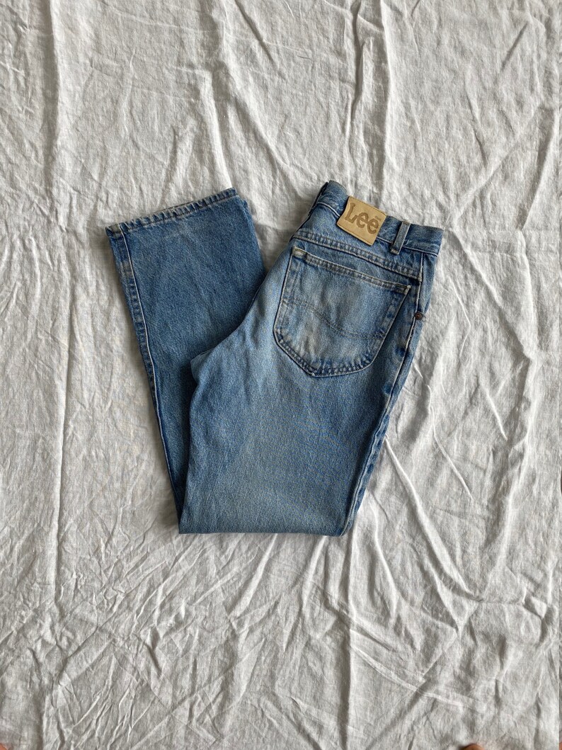 May include: A pair of blue denim jeans with a brown leather Lee label on the back pocket.